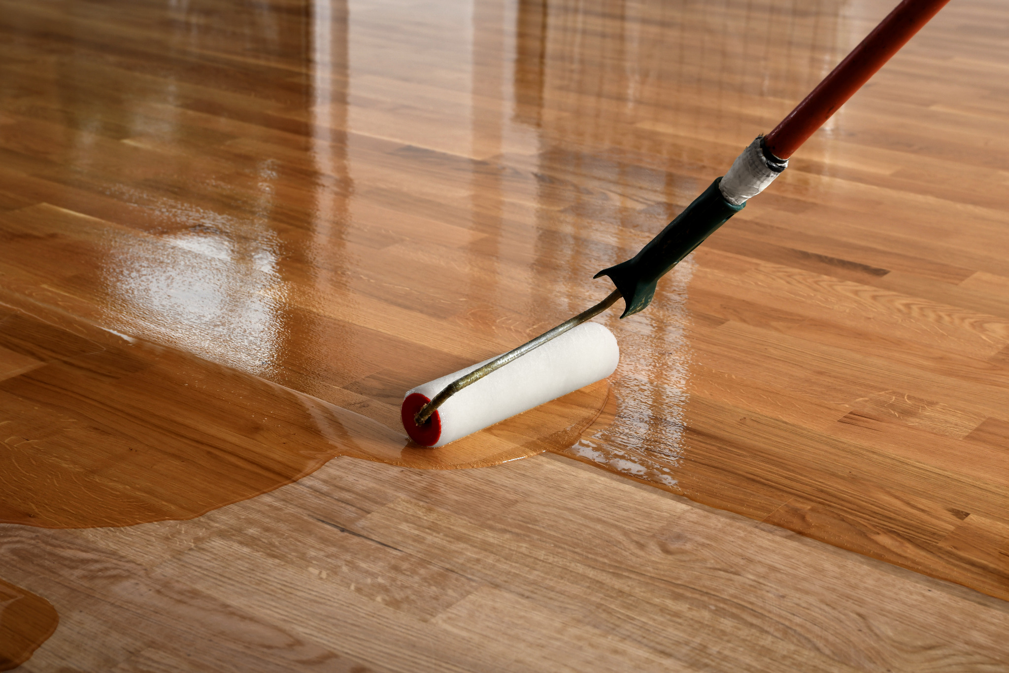 Roller applying a clear coat after the Sand Floors process on an oak hardwood plank floor, showing the wet edge and colour deepening on freshly sanded timber.