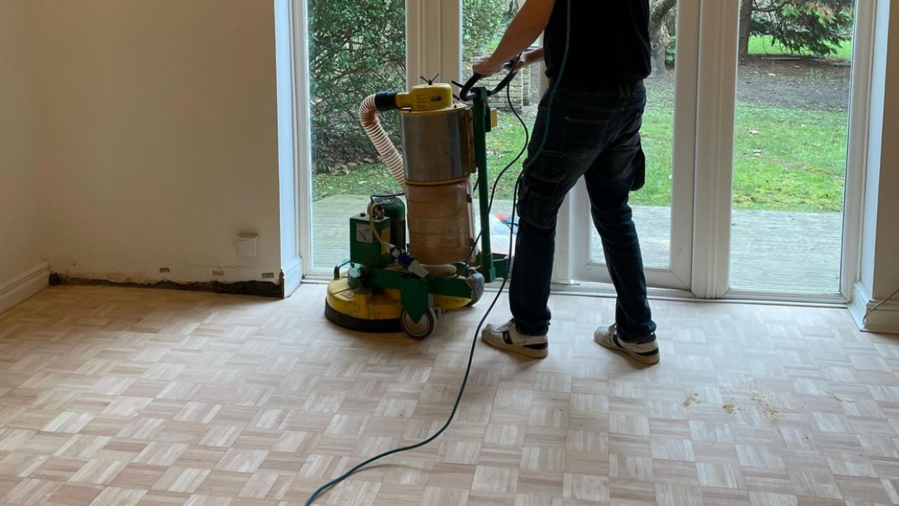 Wood Floor Sanding on pale mosaic fingers parquet hardwood flooring using a dust-free planetary sander in a living room.